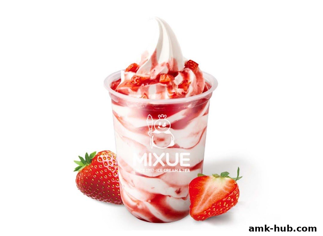 A strawberry soft serve ice cream with strawberry sauce and chunks in a clear cup, with fresh strawberries.