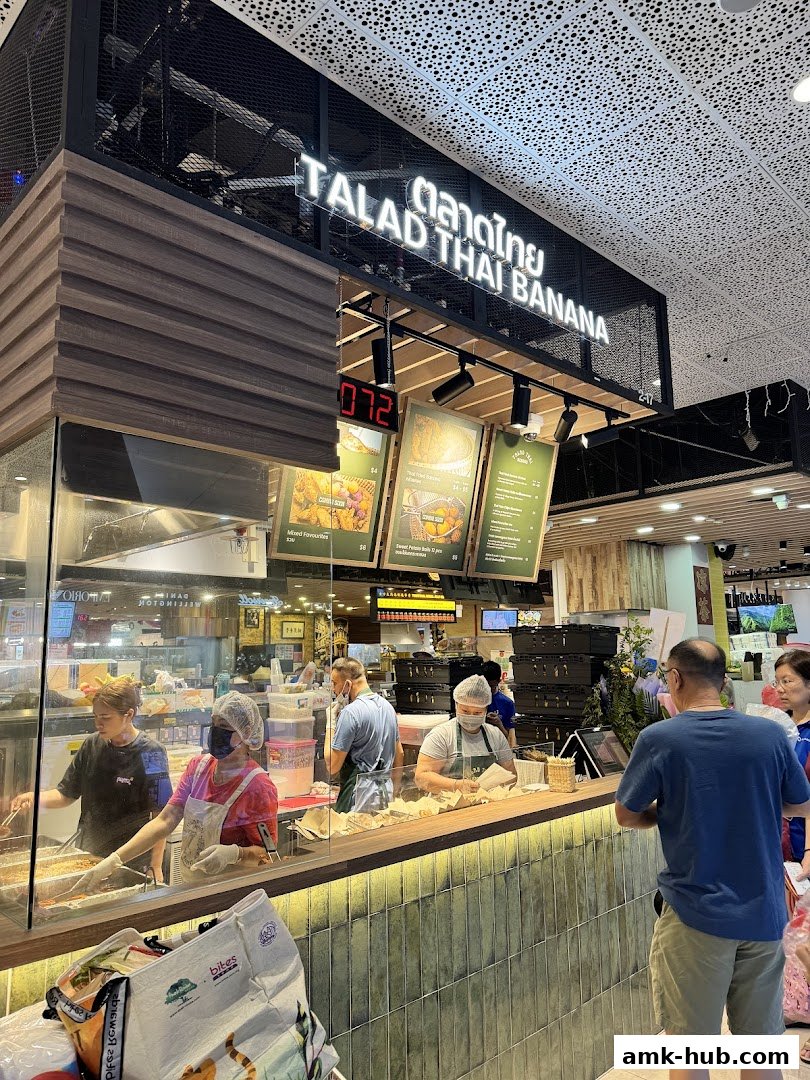 A busy Thai food stall with staff preparing orders behind a counter.