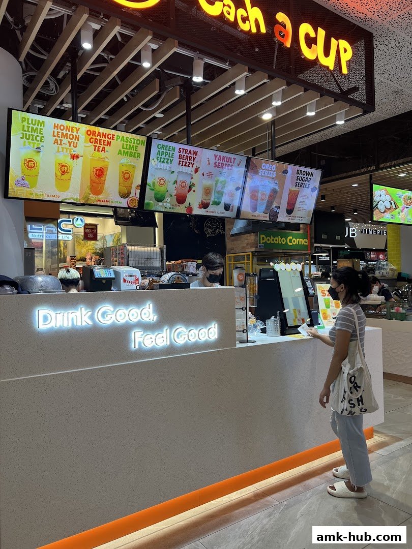A customer orders drinks at a brightly lit beverage counter with digital menus displaying colorful drinks.