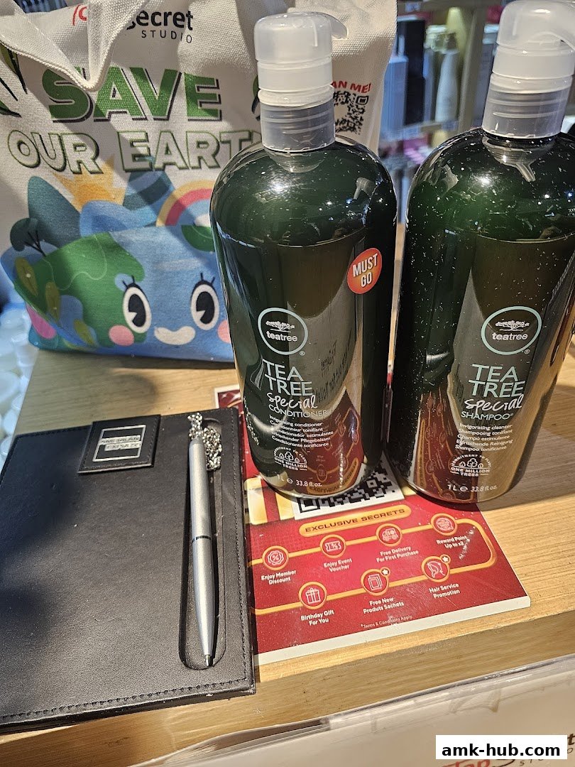 Two bottles of tea tree shampoo and conditioner, a tote bag, and a pen on a desk.