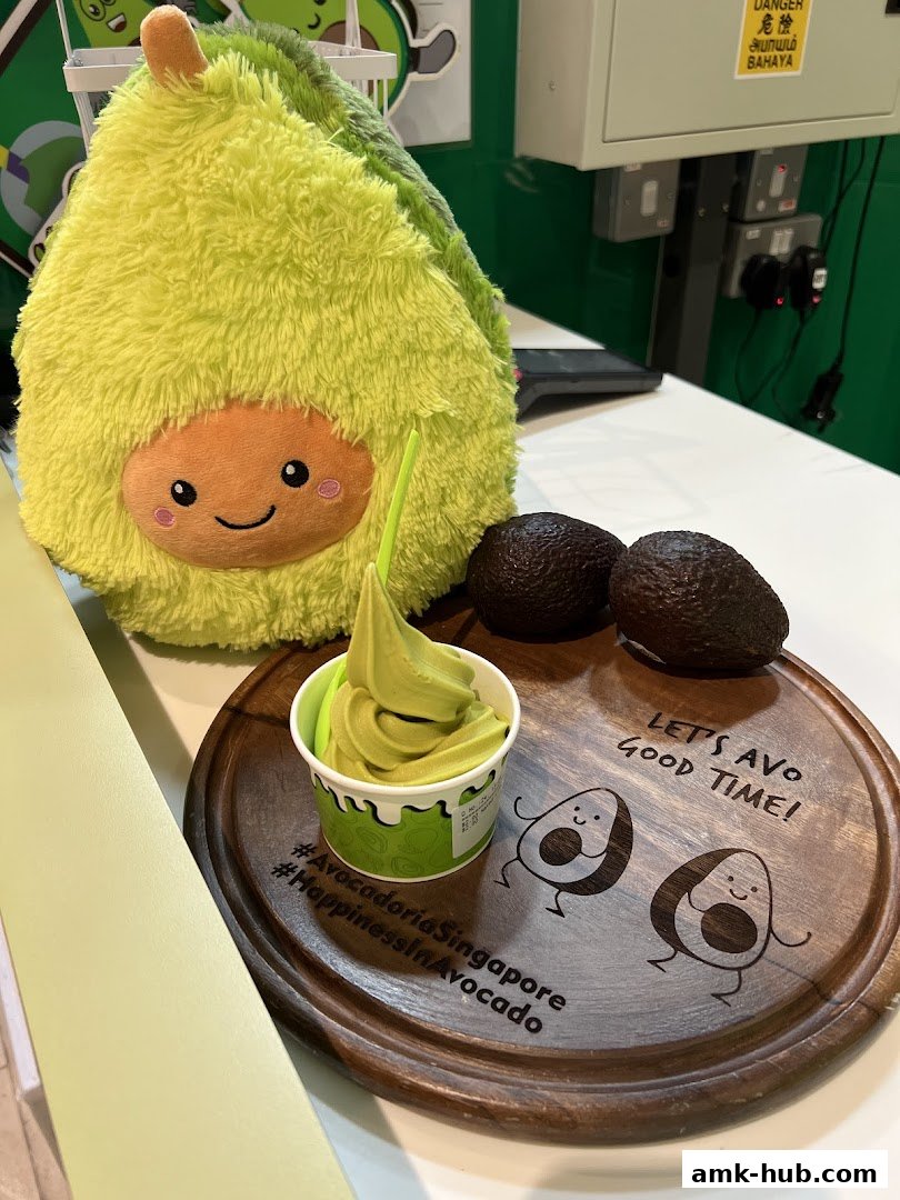 A cup of avocado soft serve ice cream with avocados and a plush toy.