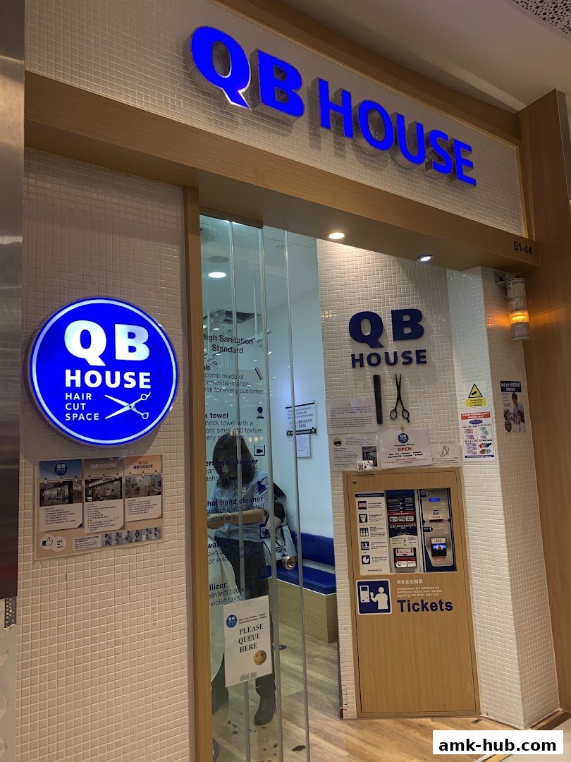 The entrance of QB HOUSE, a hair salon, with its prominent blue signage and a ticket machine.