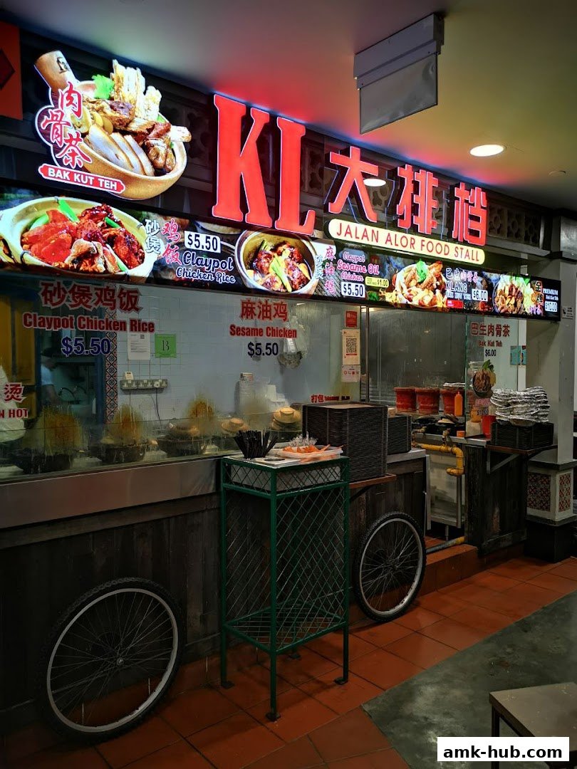A brightly lit food stall with neon signs displaying various Malaysian dishes and prices.