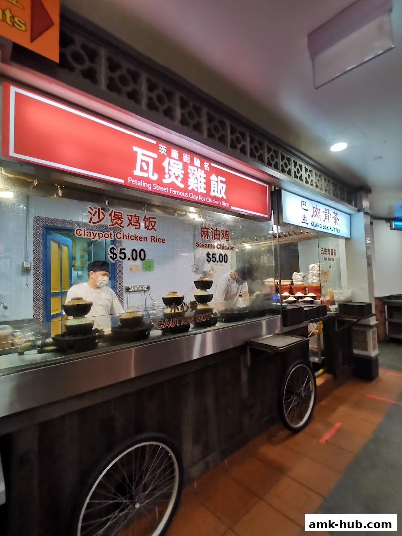 A food stall featuring claypot chicken rice and sesame chicken with prices displayed.