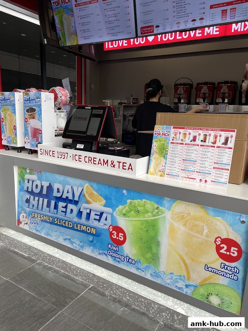 A Mixue shop counter with drinks, a menu board, and a staff member preparing orders.