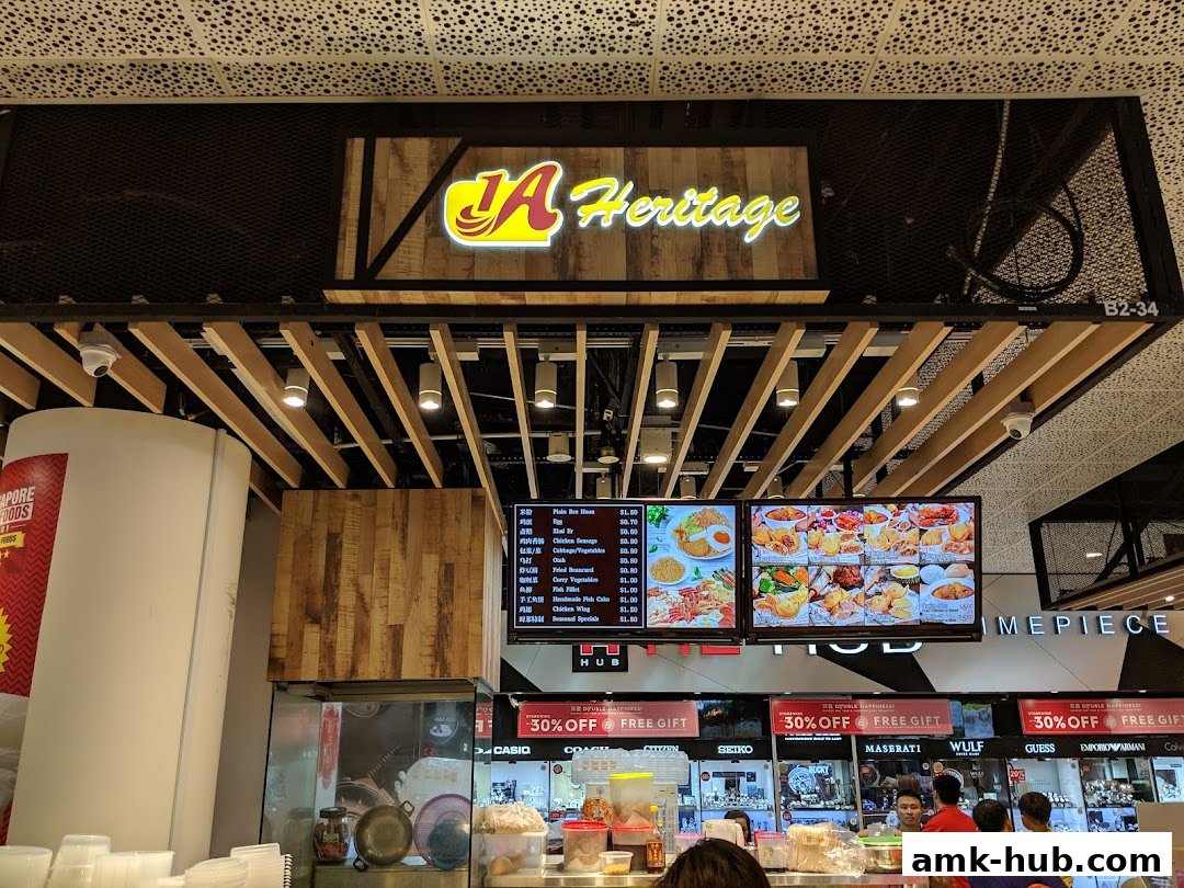 A food stall with a prominent "1A Heritage" sign and digital menus displaying food items.