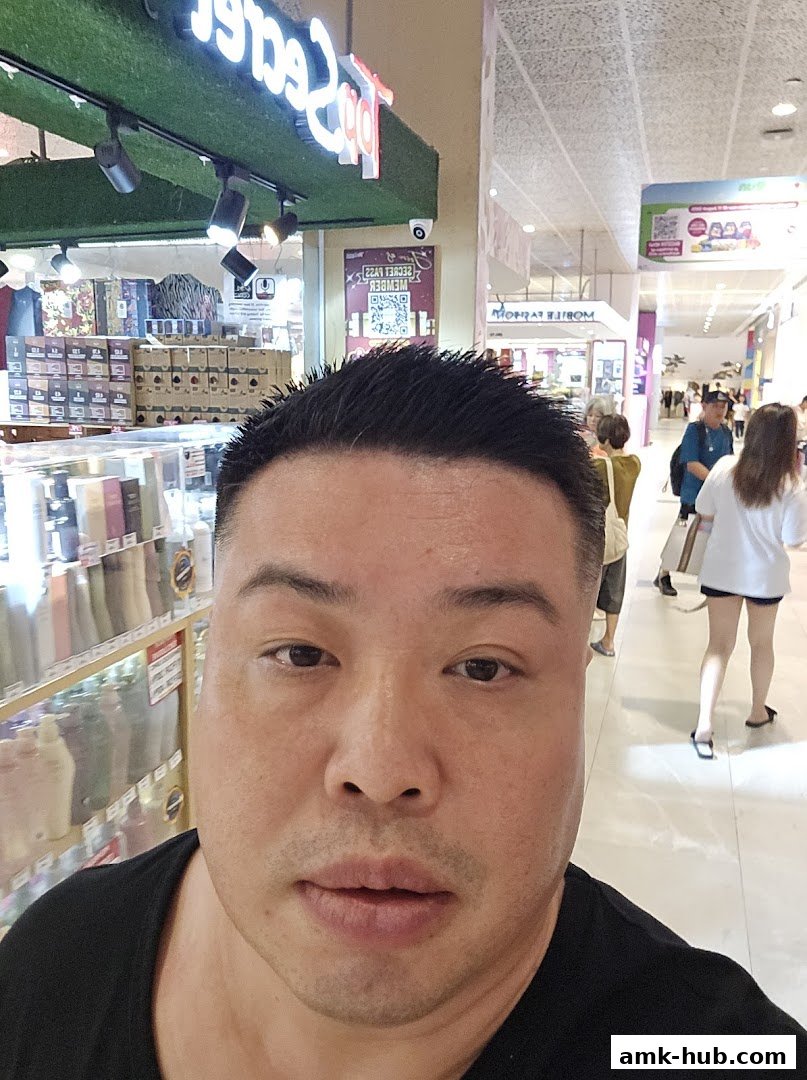 A man takes a selfie in front of a shop with products displayed on shelves.