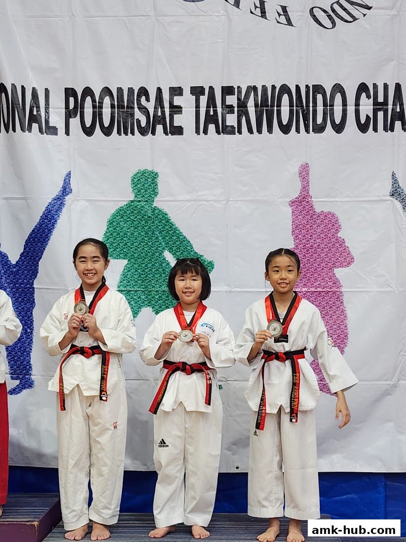 Three young girls in Taekwondo uniforms proudly display their medals at a competition.