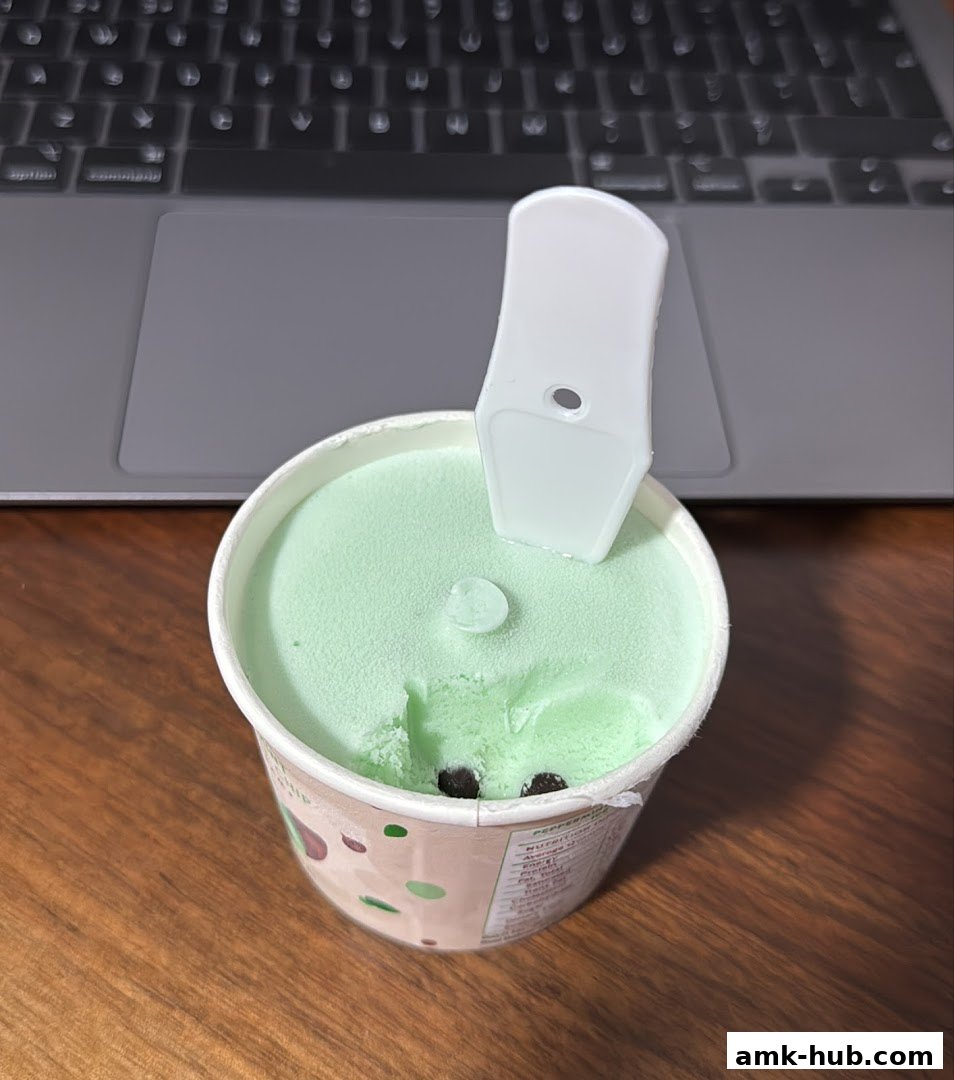 A tub of mint chocolate chip ice cream with a spoon on a wooden table.