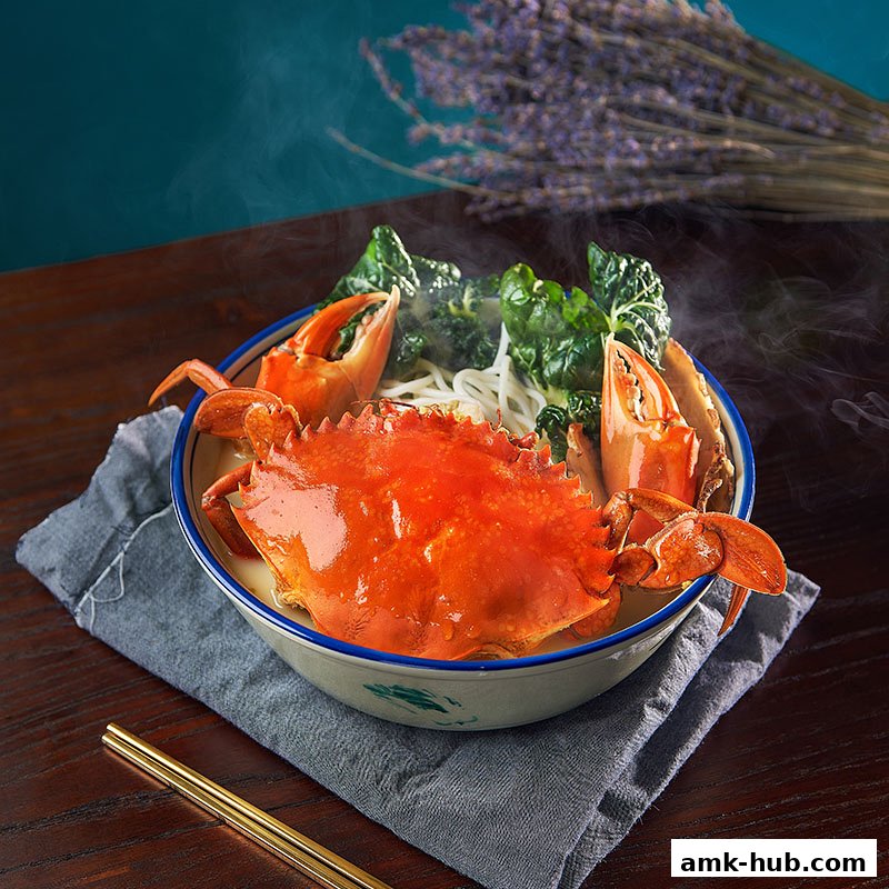 A steaming bowl of crab noodle soup with fresh greens and chopsticks on a wooden table.