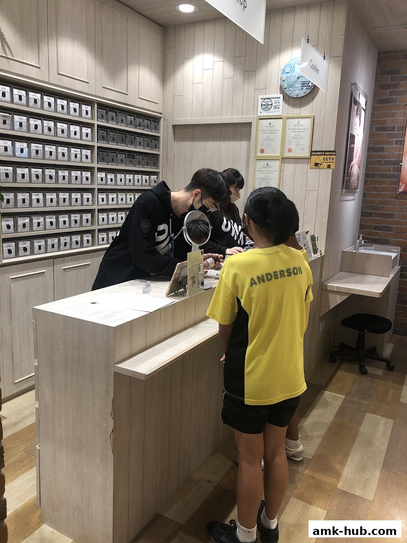 Staff assisting customers at the counter of an eyewear shop with shelves of products.