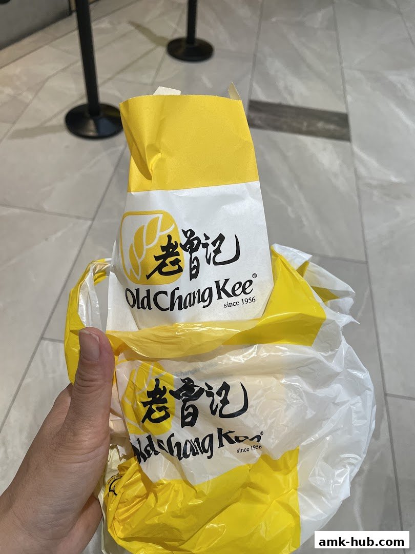 A hand holds a crumpled yellow and white paper bag with the Old Chang Kee logo.