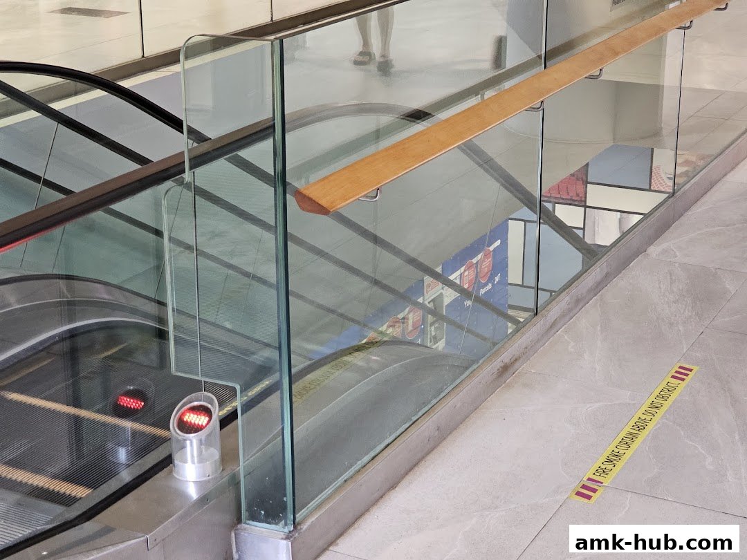 Escalator with glass railings and a safety warning sticker on the floor.