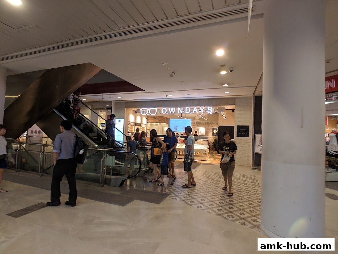 People walk past the OWNDAYS optical shop entrance with a display of glasses.