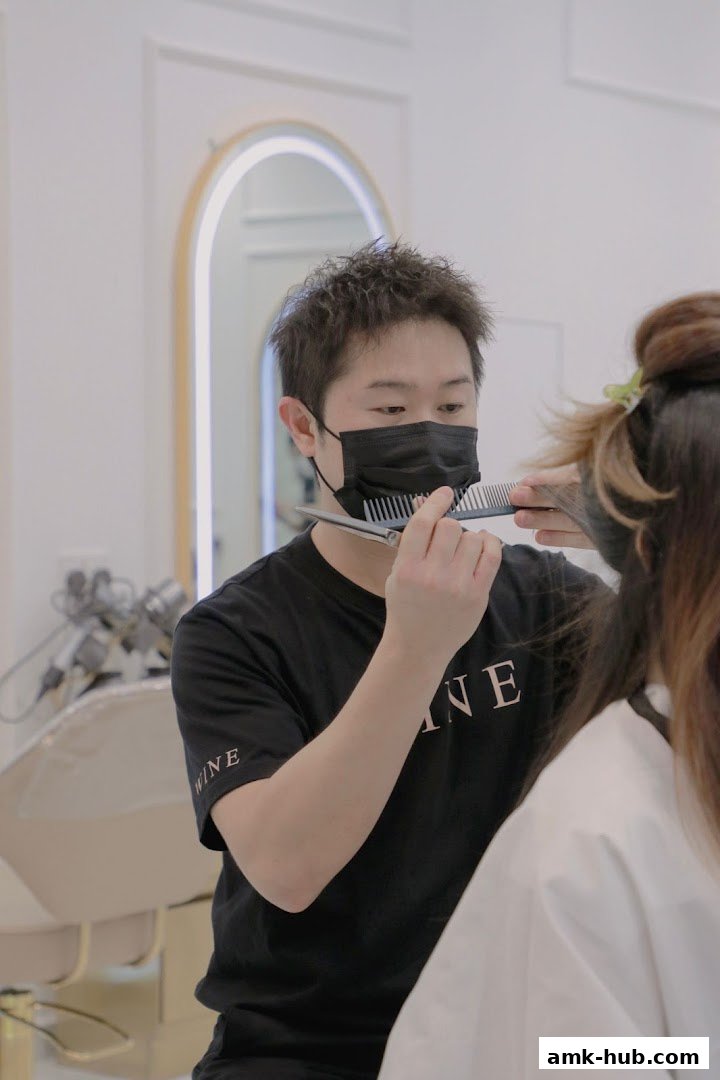A stylist with a mask cuts a client's hair in a bright, modern salon.