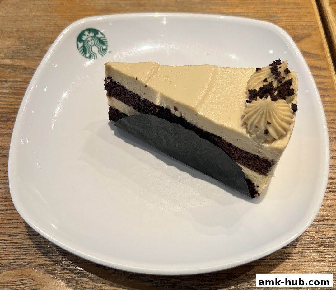 A slice of coffee-flavored cake with cream frosting and chocolate crumbles on a white plate.