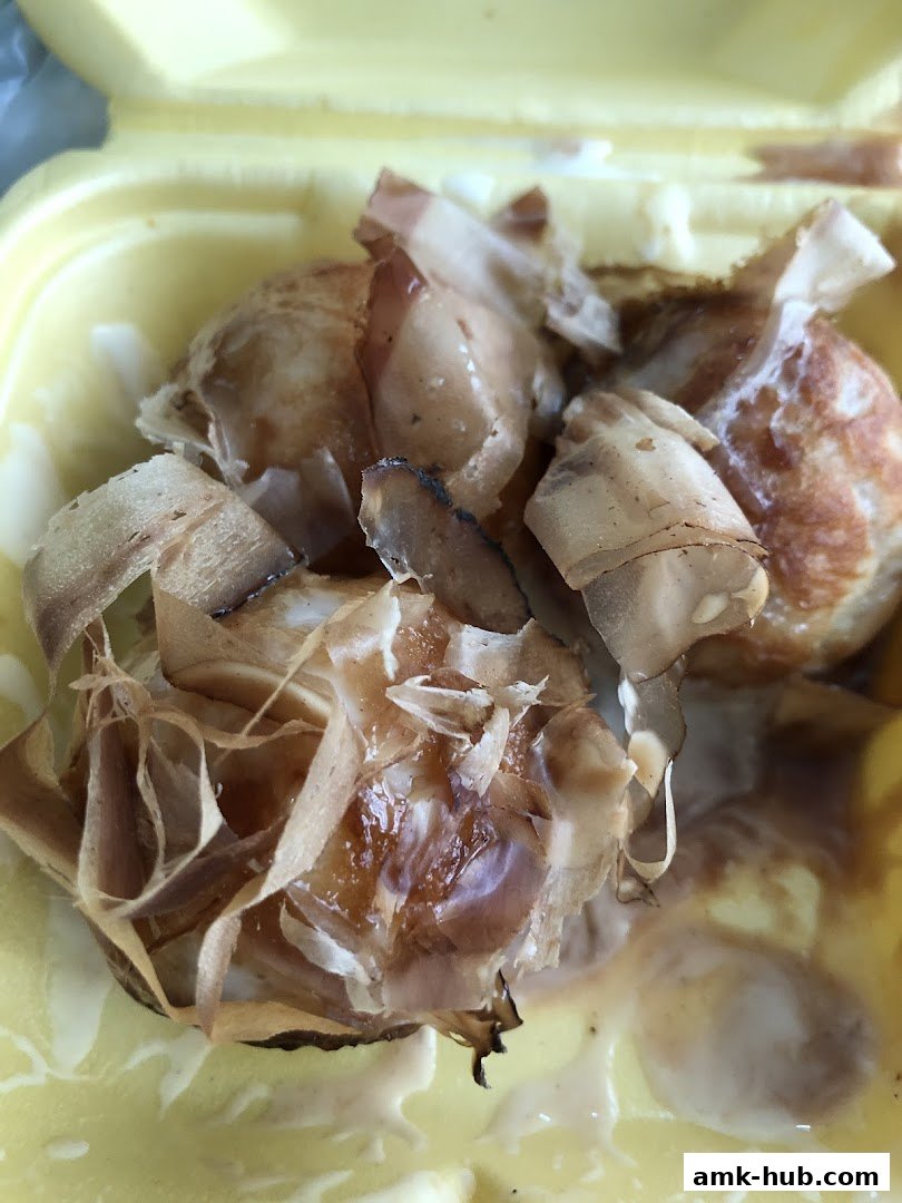 Close-up of takoyaki topped with bonito flakes and sauce in a yellow container.