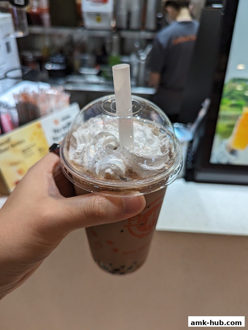 A hand holds a bubble tea with whipped cream and a straw.