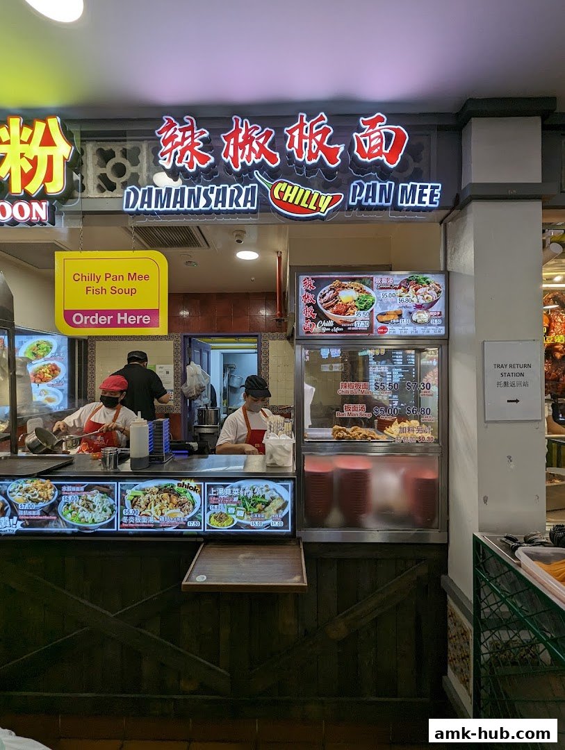 A food stall named Damansara Chilly Pan Mee with displayed menu items and staff preparing food.