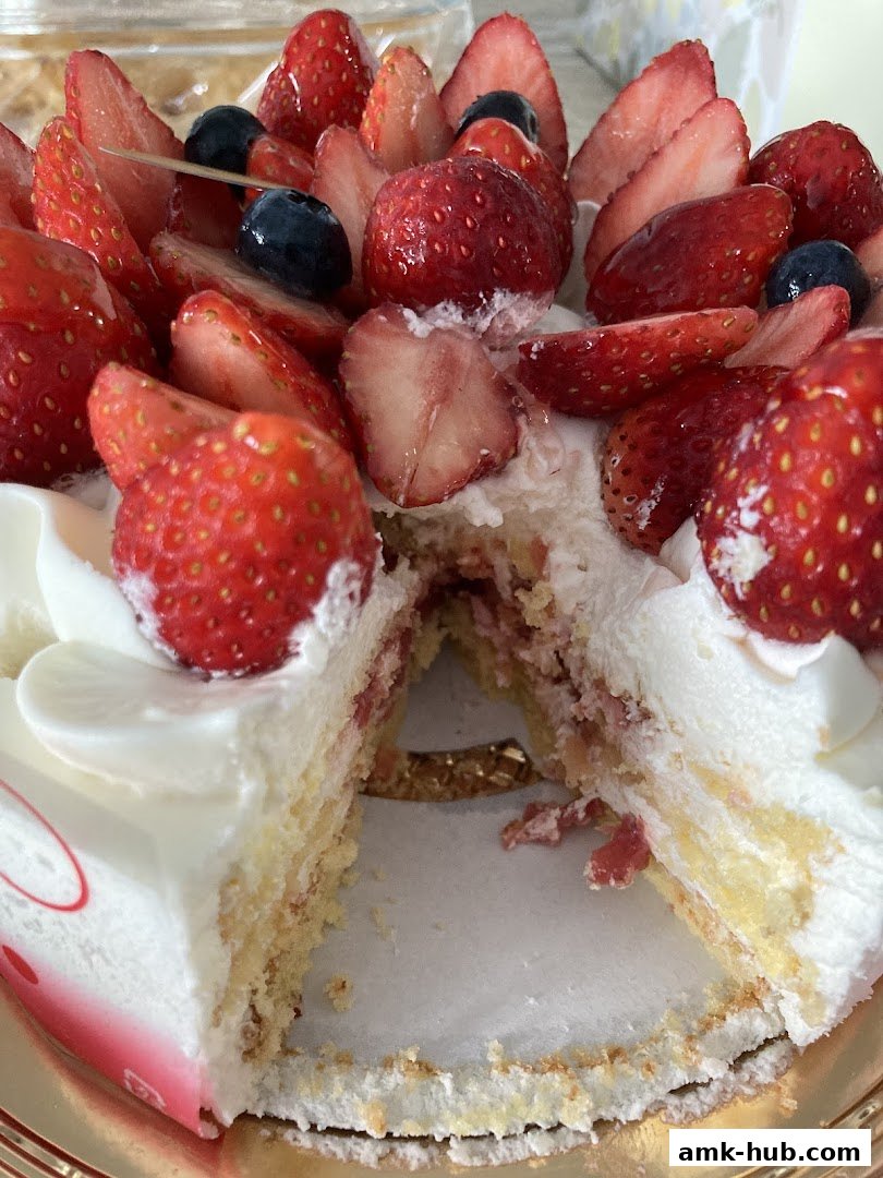 A slice of strawberry and blueberry cake with white frosting and fresh fruit.