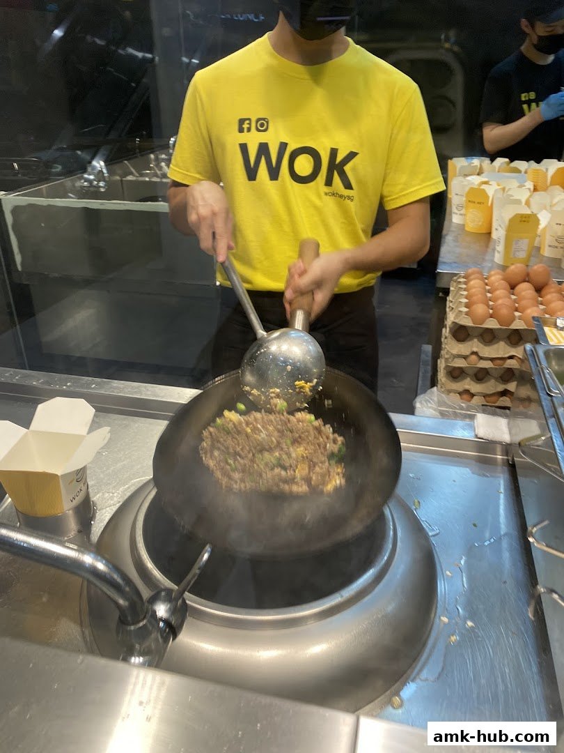 A chef in a yellow WOK t-shirt cooks fried rice in a wok.
