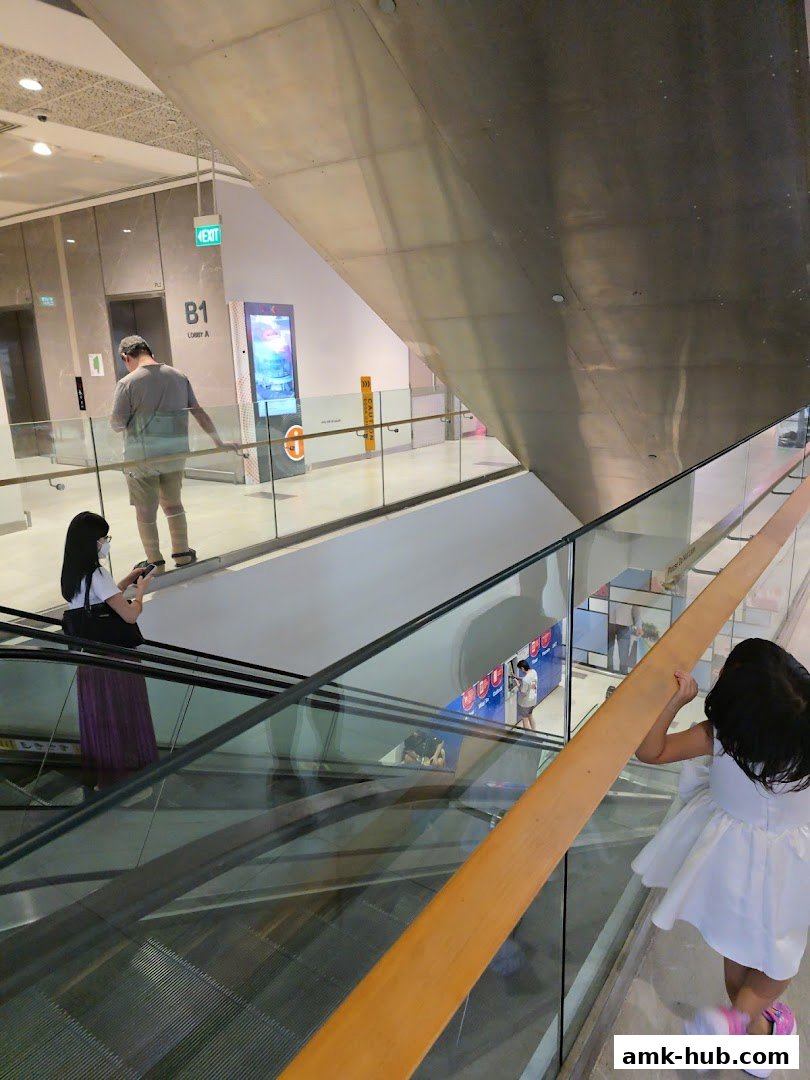 People on escalators in a modern shopping mall with glass railings and signage.