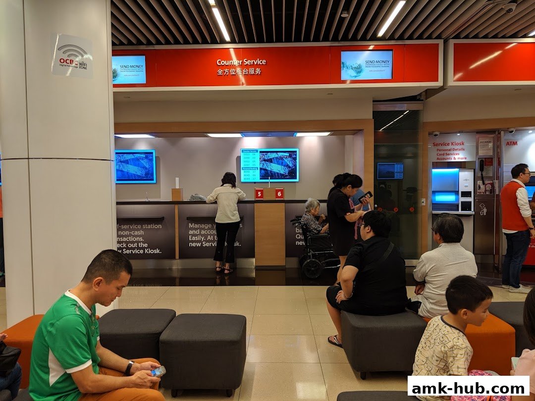People waiting at OCBC Bank for counter service and using service kiosks.
