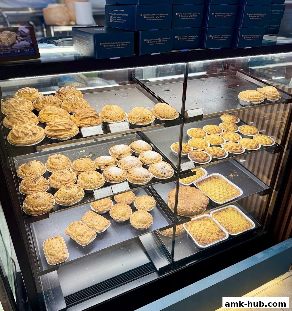 A display case filled with various freshly baked pies and pastries, with branded boxes in the background.