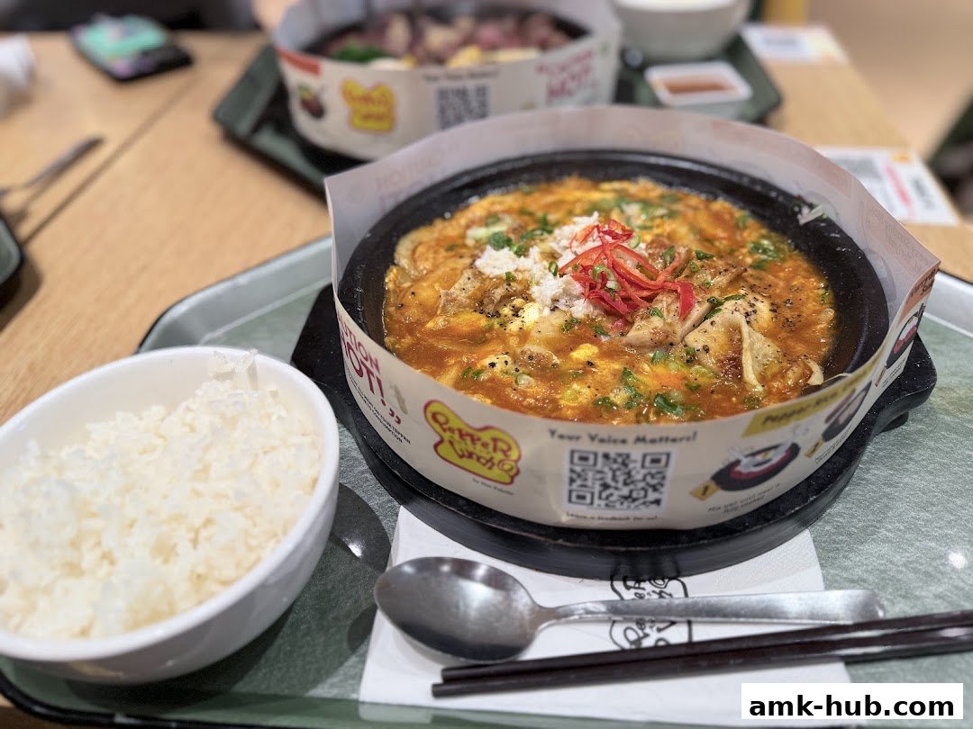 A sizzling hot plate of food with chicken and sauce, served with a side of rice.