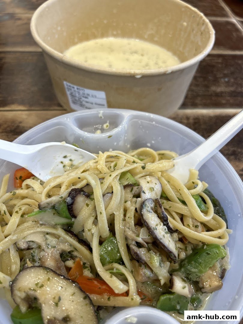 A close-up of a pasta dish with mushrooms and vegetables, served with a side of soup.