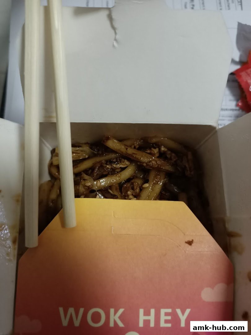 A close-up of a Wok Hey takeaway box filled with noodles and chopsticks.