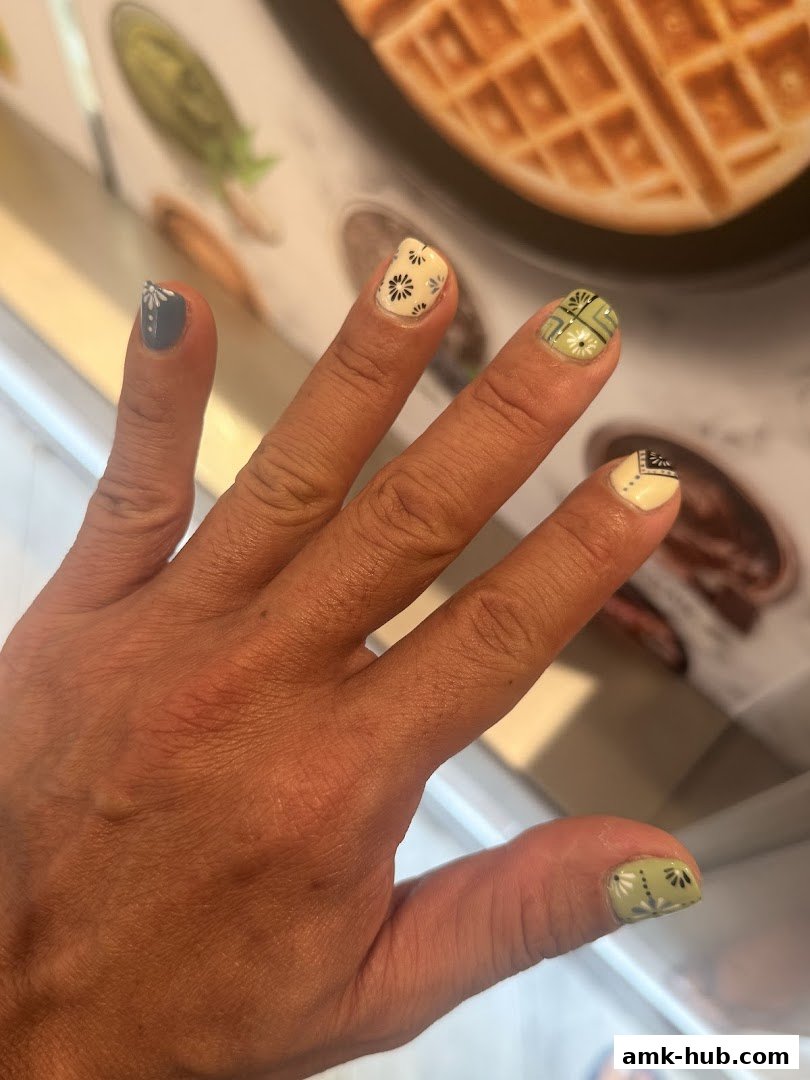 A hand with intricately designed nails featuring floral and geometric patterns.