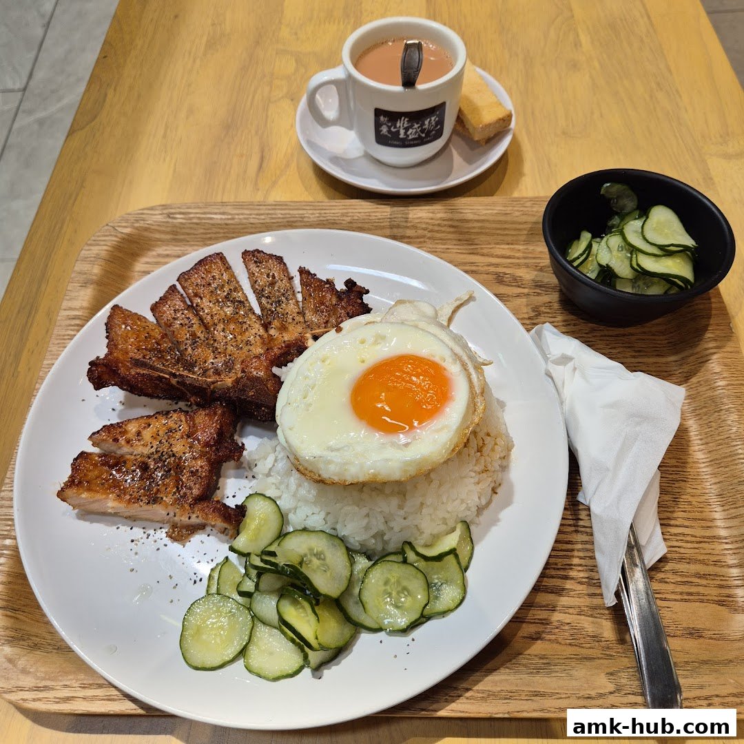 A plate of rice with fried pork chop, sunny-side-up egg, and cucumber salad, served with a cup of tea.