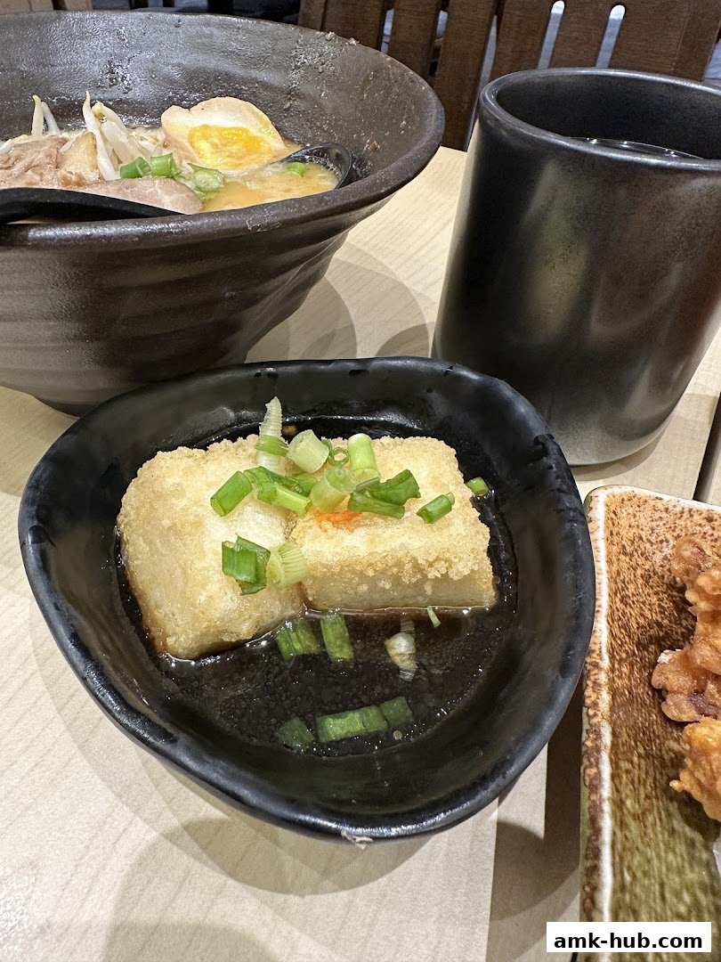 A close-up of Japanese food, including ramen, fried tofu, and a drink.