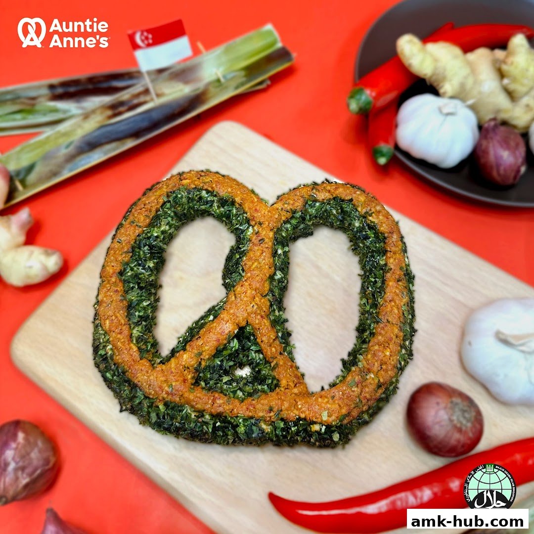 A pretzel with green and orange toppings, surrounded by ingredients like chili, garlic, and ginger.