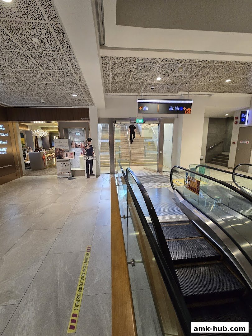 A view of a shopping mall corridor with escalators, stairs, and shop entrances.