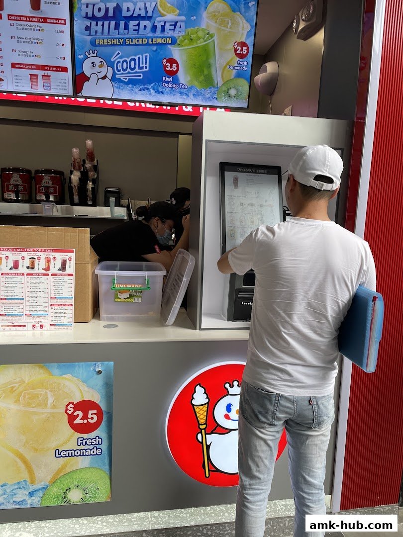 A customer orders at a MIXUE ice cream and tea shop with a digital menu and promotional posters.