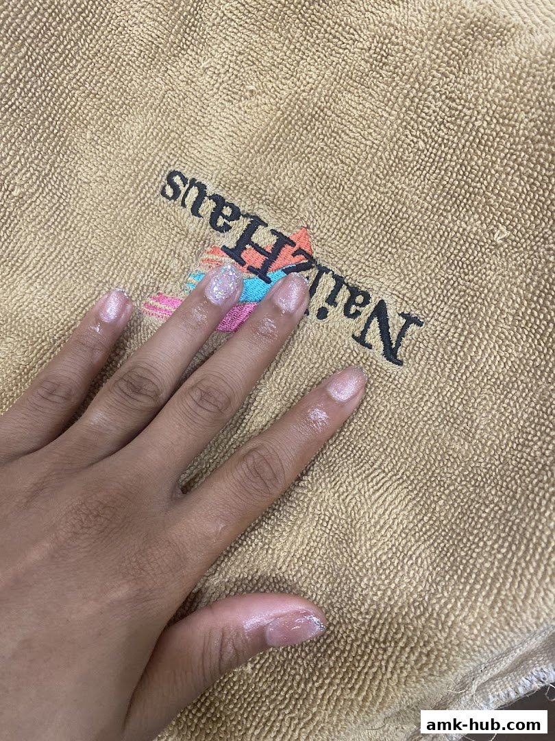 A hand with freshly done glittery nails rests on a textured towel with the Nailz Haus logo.