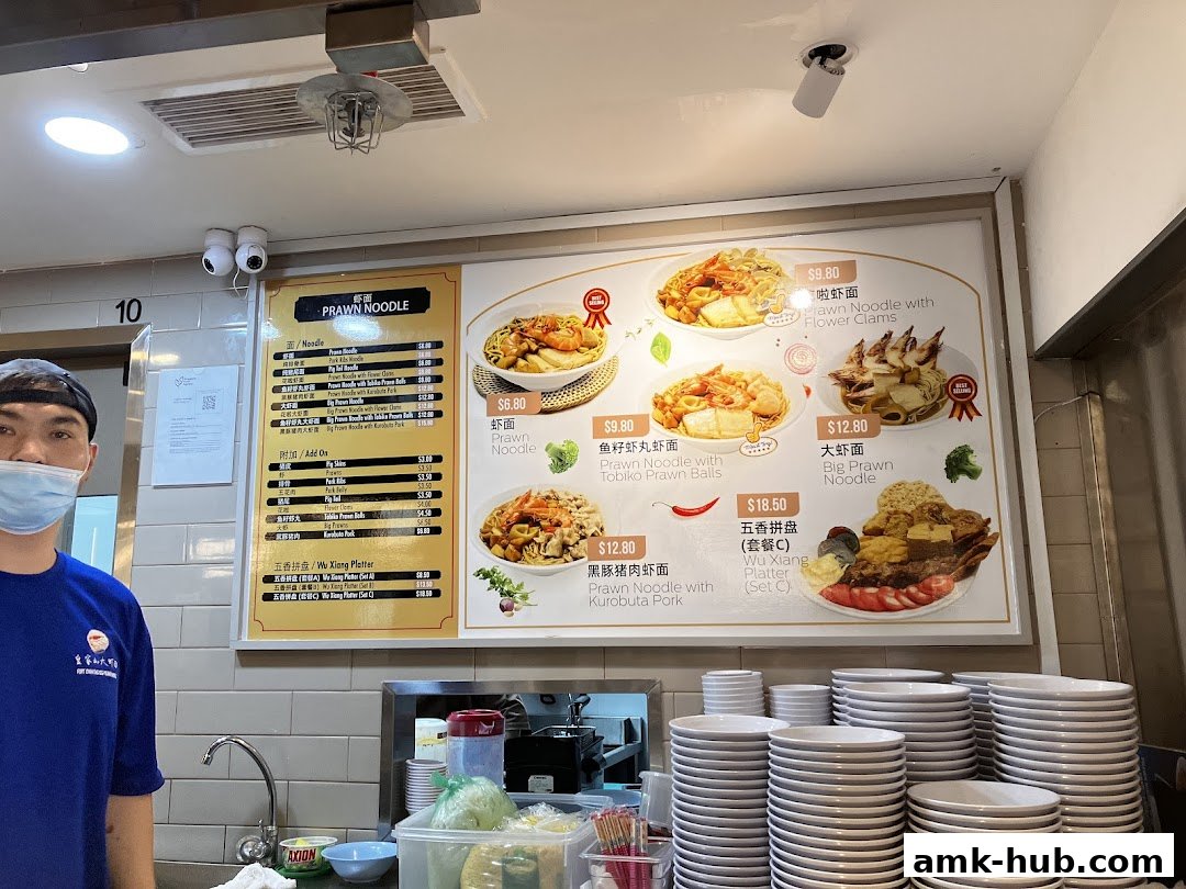 A menu board displays various prawn noodle dishes and platters with prices.