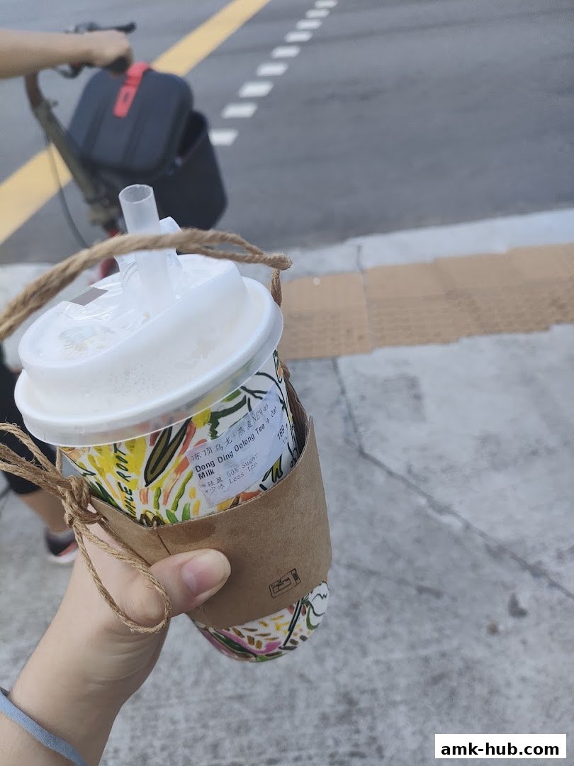 A hand holds a takeaway cup with a colorful design and a brown sleeve.
