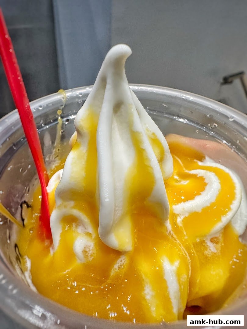 A close-up of a delicious soft-serve ice cream with mango sauce and a red spoon.