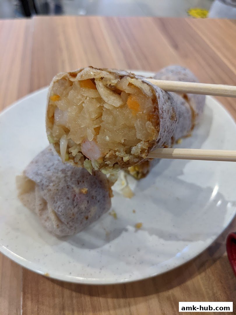 A close-up shot of a delicious popiah, held by chopsticks, showcasing its fresh ingredients.