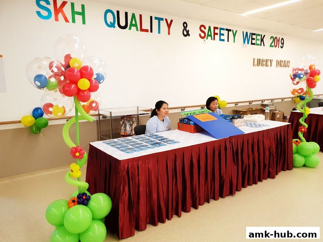 Two women at a table decorated with balloons for a 'Quality & Safety Week' event.