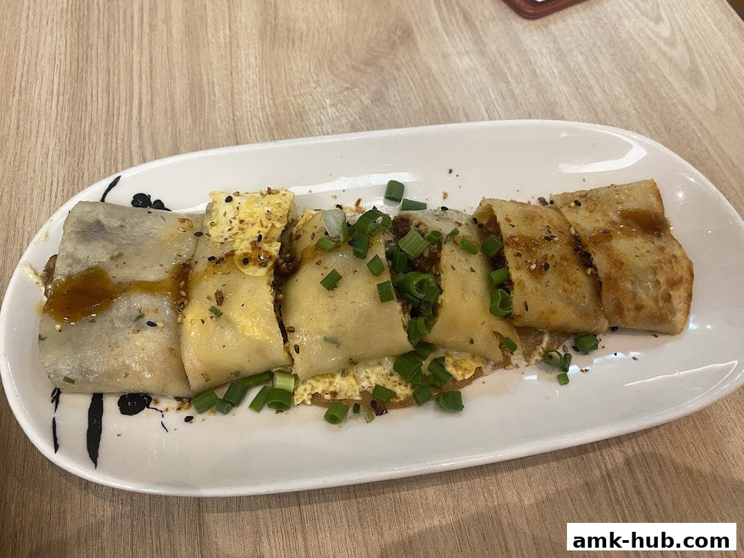 A plate of sliced savory crepes filled with meat and topped with scallions and sesame seeds.
