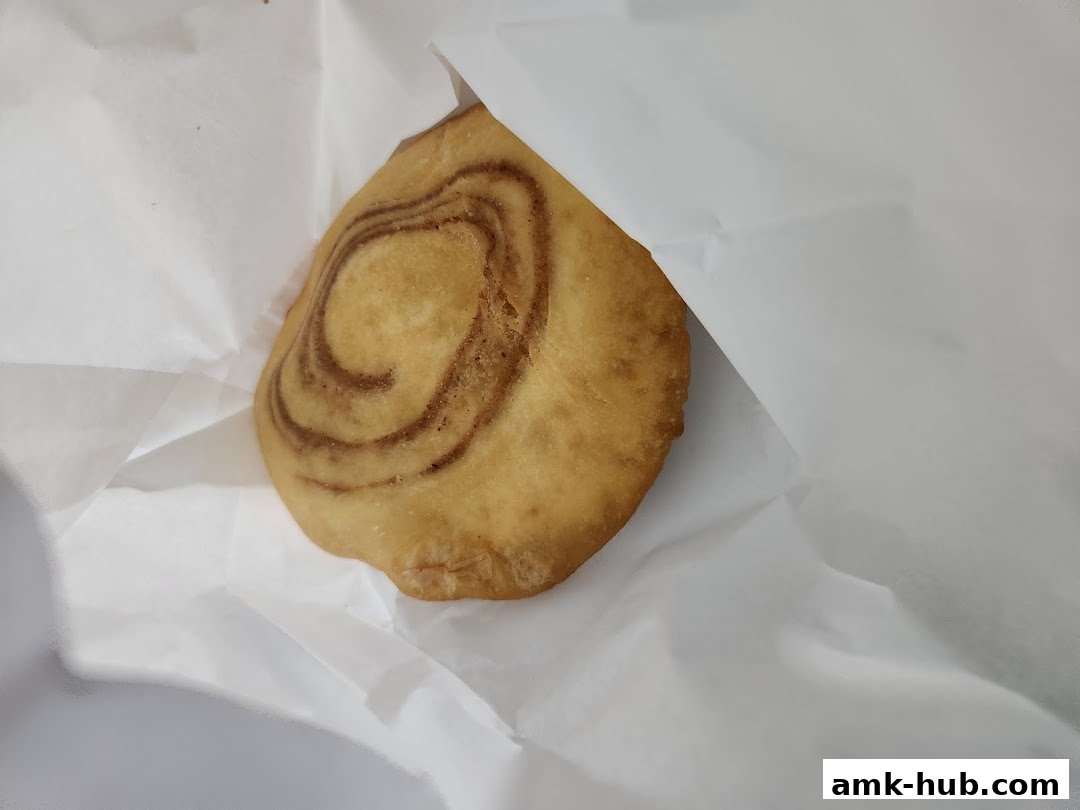 A close-up shot of a freshly baked cinnamon swirl pastry wrapped in white paper.