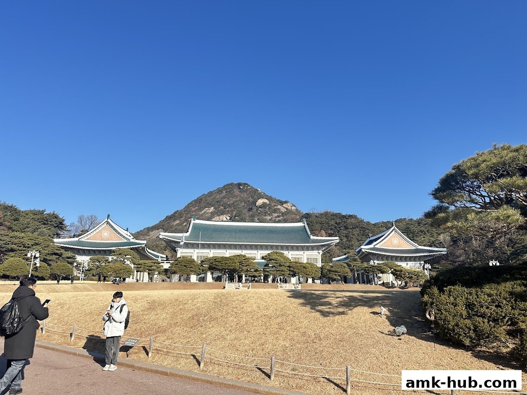 A wide shot of traditional Korean buildings with green roofs against a clear blue sky.