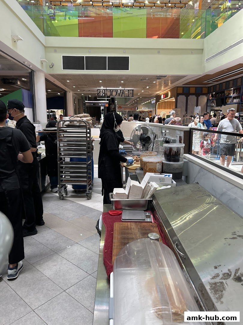 Staff preparing food behind a counter in a busy shopping mall.