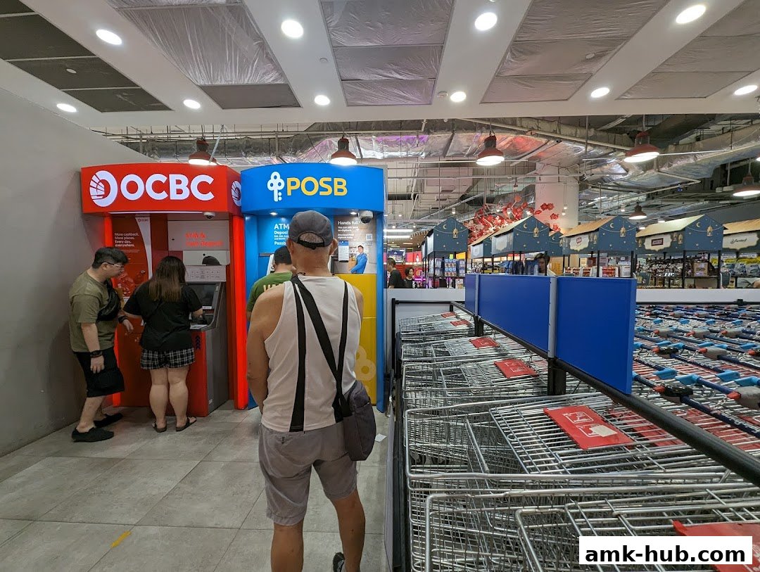 People using OCBC and POSB ATMs in a shopping mall with rows of shopping carts.