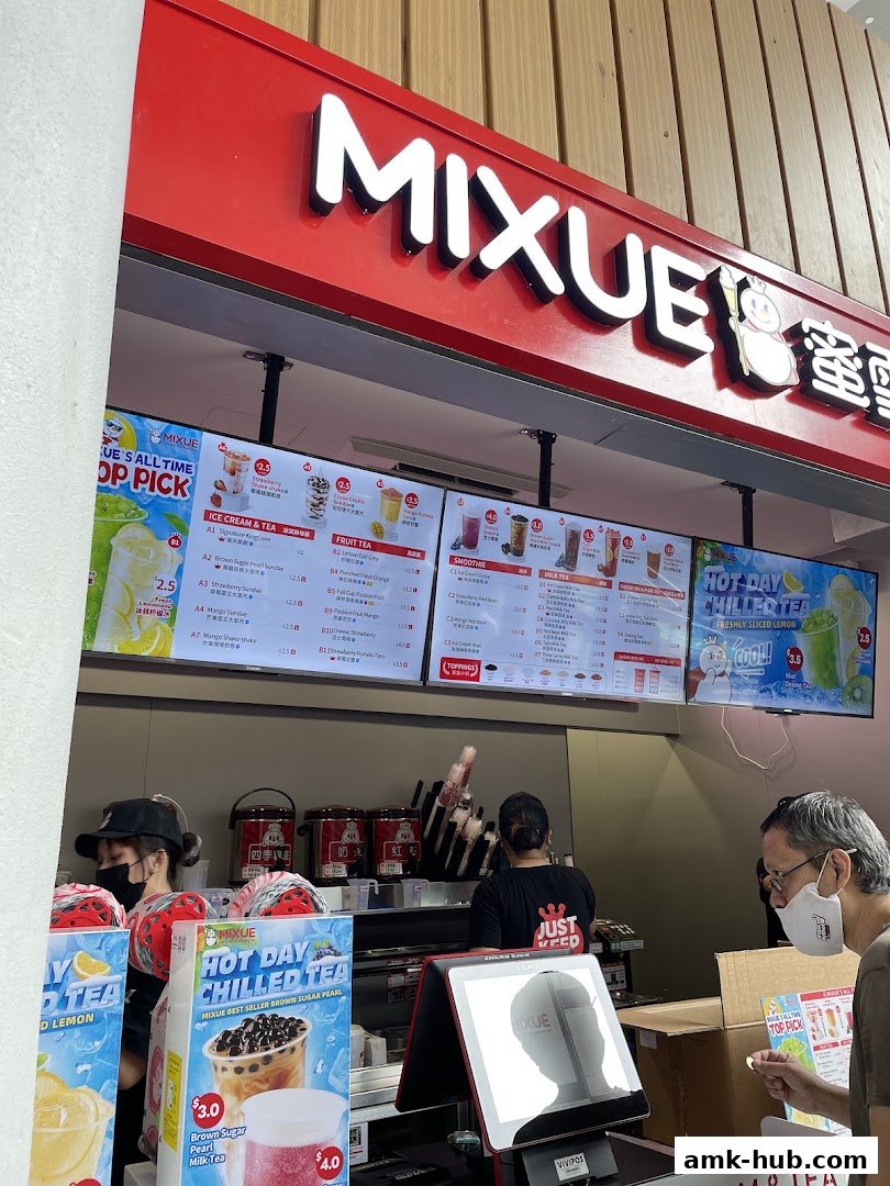 A Mixue shop counter with digital menus displaying drinks and staff serving customers.
