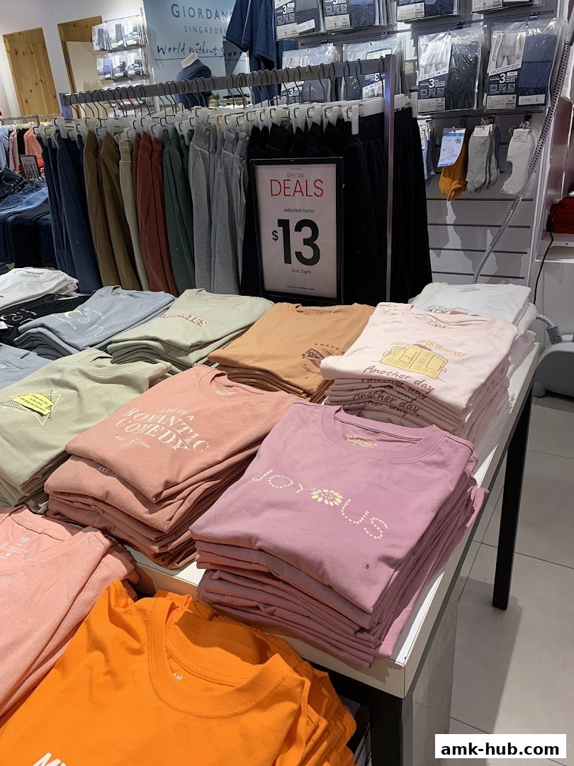 A display of folded t-shirts in various colors and styles, with a promotional sign for special deals.